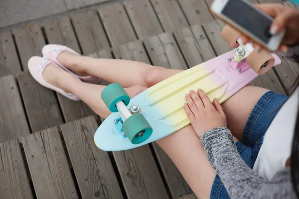 Menina tira foto de pernas e skate no telefone inteligente — Fotografia de Stock