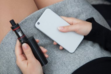 Buharlaştırıcı ve modern akıllı telefon tutarak kız