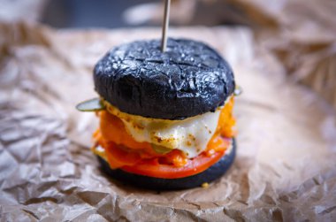 Fast food lokantası menülerinde kahverengi kağıda servis edilen sığır pirzolası, sos, peynir ve marul salatası ile büyük siyah hamburger. Fast food kafe mutfağı sağlığa zararlıdır ama çok lezzetlidir.