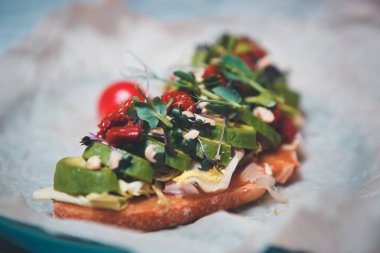 Lezzetli avokado sandviçi, kurutulmuş domatesler, parşömen kağıdında mikro yeşiller vejetaryen kafeteryasında. Lezzetli vejetaryen yemekleri, sağlıklı doğal malzemelerle öğle yemeği için hazırlandı. İtalyan bruschetta.