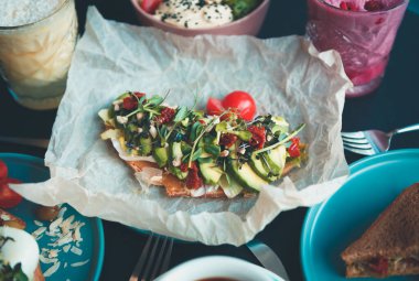 Avokado, kurutulmuş domates, bruschetta üzerinde mikro yeşiller vejetaryen restoranında öğle yemeği için el yapımı kağıt tabakta servis ediliyor. Doğal malzemeyle pişirilmiş sağlıklı vegan kahvaltı.