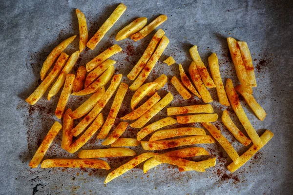Baking French fries on parchment paper in home kitchen.Delicious golden potato chips prepared for dinner in oven.Tasty natural vegetable dish cooked with smoked paprika powder spice