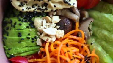 Kahvaltı için karıştırma kabı. Doğal vejetaryen malzemelerle hazırlanmış sağlıklı öğle yemeği videosu: Kore havucu, humus, dilimlenmiş avokado, salatalık, domates. Güzel egzotik yemek görüntülerinin yakınlaştırılması. 