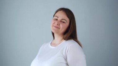 Kamerada gülümseyen ve gülümseyen güzel, büyük beden bir manken. 30 'lu yaşların başındaki çekici genç bir kadının beyaz gömlek giyip stüdyoda neşeli bir yüz ifadesi ile poz verdiğinin portresi.