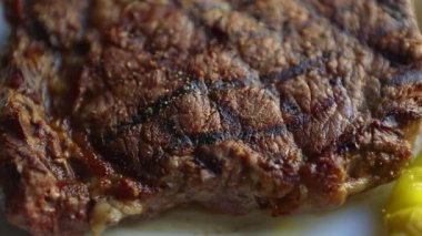 Restoranda akşam yemeği için ızgara biftek. Izgarada pişmiş, beyaz seramik tabakta servis edilmiş, yukarıdan zoom etkisi ile filme alınmış lezzetli sığır eti. Gurme kırmızı et filetosu yemek için hazır.