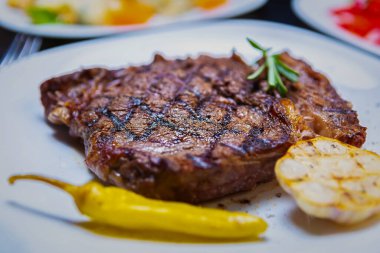 Restoranda akşam yemeği için ızgara biftek. Izgarada pişirilmiş lezzetli et, beyaz seramik tabakta servis ediliyor.