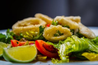 Kızarmış kalamar halkaları ve kafede öğle yemeği için taze marul salatası. Kahvaltı için fritözde pişirilmiş lezzetli Akdeniz ürünleri. Beyaz tabakta gurme kalamar ızgarası.