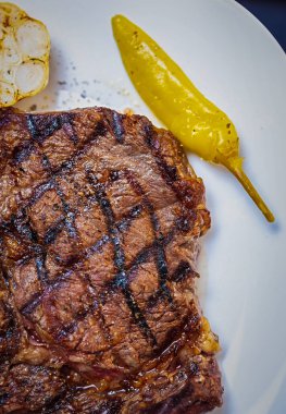 Düz katlı ızgara kaburga bifteği. Akşam yemeğinde ızgarada pişirilmiş Amerikan bifteği. Beyaz seramik tabakta acı biberle servis ediliyor.
