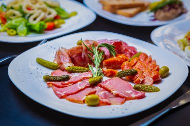 Şarap aperatifleri için sunulan mezeler: dilimlenmiş jambon, İspanyol jamonu, tütsülenmiş pepperoni sosisi, salatalık turşusu, biberiye otu. Akdeniz restoranındaki aperatif yemekler yakın planda.