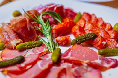 Restoranda parti için nefis aperatifler. Tabakta servis edilen et atıştırmalıkları: dilimlenmiş jambon, İspanyol jamonu, tütsülenmiş salatalık ve salatalık turşusu.