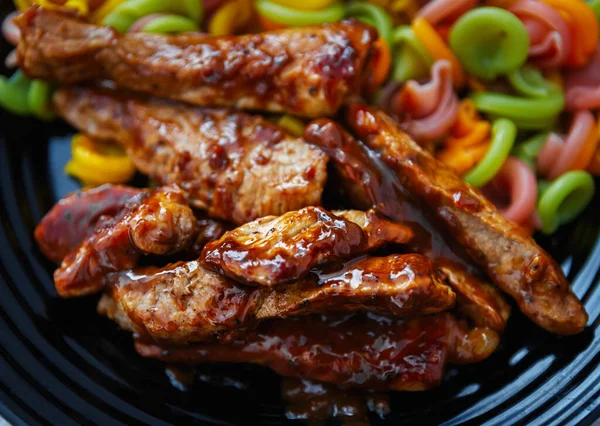 Akşam yemeği için karamel sosunda pişirilmiş biftek, siyah seramik tabakta renkli İtalyan makarnası. Restoranda öğle yemeği için hazırlanmış lezzetli domuz eti şeritleri. Baharatlı kızarmış yemeğin tadını çıkarın.