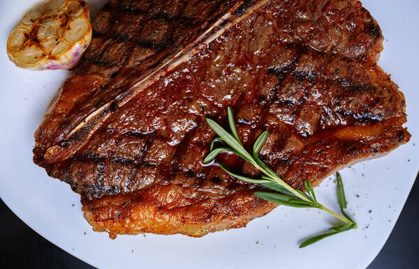 Delicious meat steak in flat lay.Gourmet beef sirloin on bone cooked on grill,served on white ceramic plate in restaurant.Tasty natural piece pork meat grilled for dinner,shot directly from above