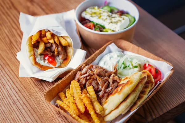 Fast food delivery.Greek souvlaki,salad &gyros take away menu from fastfood restaurant served in recyclable paper plates on table.Delicious sandwiches,french fries,white tzatziki sauce delivered order