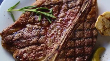 Restoranda akşam yemeği için ızgara biftek. Izgarada pişmiş, beyaz seramik tabakta servis edilmiş, yukarıdan zoom etkisi ile filme alınmış lezzetli sığır eti. Gurme kırmızı et filetosu yemek için hazır.