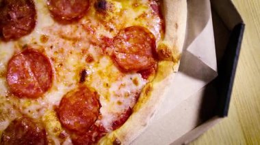 Karton kutuda İtalyan biberli pizza teslimatı. Yukarıdan çekilen geleneksel fast food çekimlerinin en üst görüntüsü. Erimiş peynirli ince hamurlu fırında pişirilmiş füme sosis.