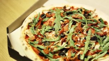 Vejetaryen pizzası roka salatası, pesto sosu, kurutulmuş domates, fırında pişmiş siyah zeytin kabuklu ince hamur tabakası. Sağlıklı ve doğal fast food teslimatı. Akşam yemeği için paketlenmiş pizza görüntüleri. 