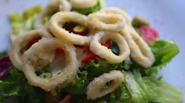 Lezzetli deniz ürünleri salatası. Kızartma makinesinde kızartılmış mürekkep balığı soğanı taze marul yaprakları, limon ve Akdeniz restoranında beyaz tabakta domatesle servis ediliyor. İtalya 'da pişirilen lezzetli deniz ürünleri mutfağı