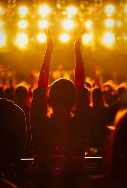 Silhouette of young girl waving hands to the music on popular dj concert in night club.Big group of people partying on electronic musical festival