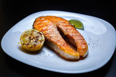 Izgarada pişirilmiş kırmızı balık fileto. Akşam yemeğinde ızgara somon bifteği. Limonlu beyaz tabakta servis ediliyor.