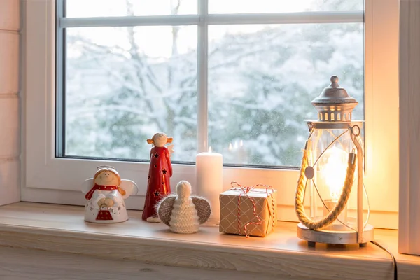 Latarnia bożonarodzeniowa, anioły z prezentami na oknie drewnianego domu z widokiem na ogród zimowy w nocy w zimie. — Zdjęcie stockowe