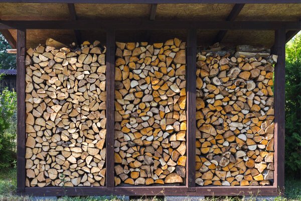 They prepare firewood for heating in winter. Firewood is neatly stacked under the roof of the shed for heating.