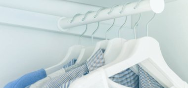 Askılarda açık mavi gömlekler ve bluzlar asılı beyaz gardırop.