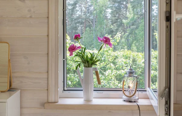 Ventana blanca con mosquitero en una casa de madera rústica con vistas al jardín. Ramo de peonías rosadas en una regadera en el alféizar de la ventana — Foto de Stock