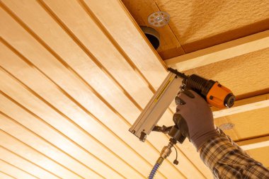 İç yenileme sırasında ahşap tavan panellerini güvence altına almak için pnömatik çivi tabancası kullanan işçiler, kereste inşaat süreci, izolasyon katmanları, el işçiliği, işçilik ve kusursuz ev geliştirme çalışmaları