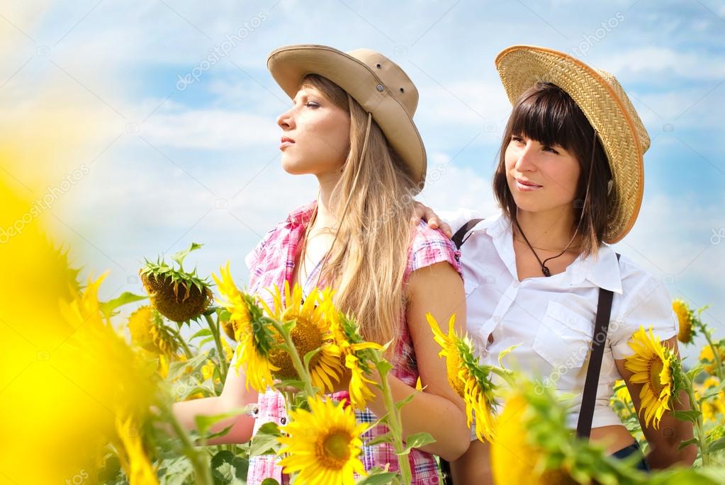 Beautiful Girls in a Cowboy Hats at the Sunflowers Field. 