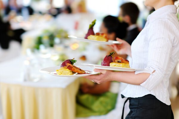 Waitress carrying three plates with meat dish