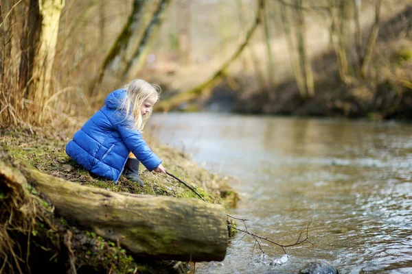 Dívka si hraje s holí u řeky — Stock fotografie