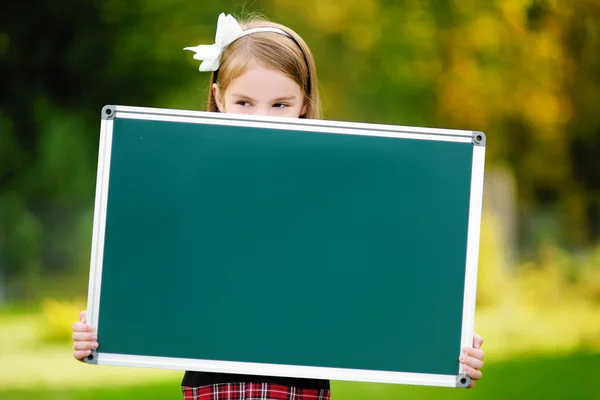 Liten skolflicka innehar en svarta tavlan — Stockfoto
