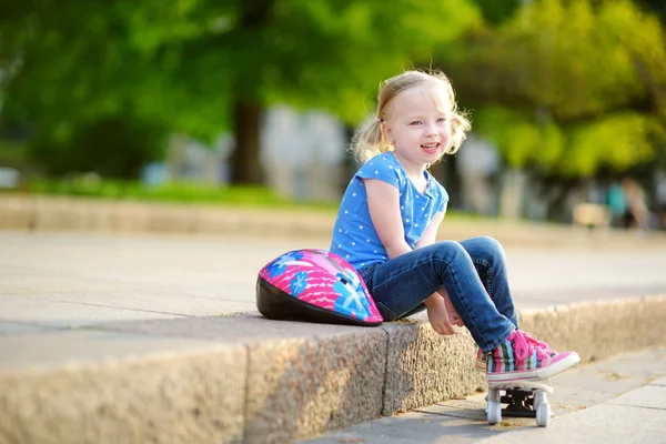 Маленькая девочка сидит на скейтборде — стоковое фото