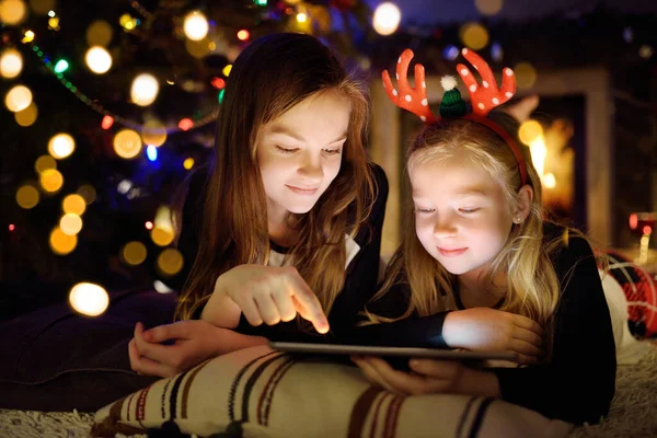 Two Cute Young Sisters Using Tablet Home Fireplace Warm Cozy — Stock Photo, Image