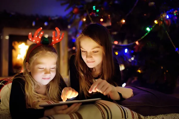 Two Cute Young Sisters Using Tablet Home Fireplace Warm Cozy — Stock Photo, Image