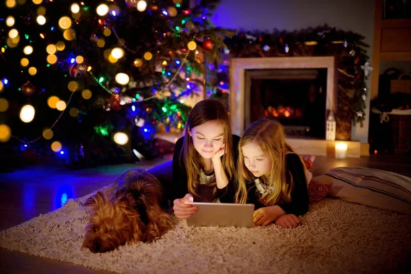 Two Cute Young Sisters Using Tablet Home Fireplace Warm Cozy — Stock Photo, Image