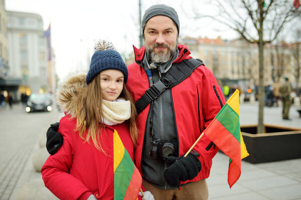 Father and daughter holding tricolor Lithuanian flag on Lithuanian Independence Day in Vilnius. Happy family celebrating national holiday.