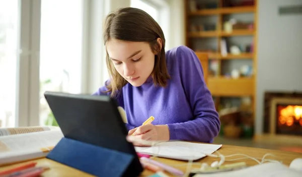 Preteen schoolgirl doing her homework with digital tablet at home. Child using gadgets to study. Education and distance learning for kids. Homeschooling during quarantine. Stay at home entertainment.