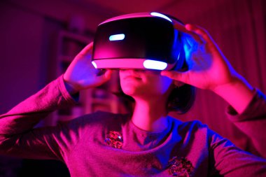 Karanlık bir odada sanal gerçeklik kulaklığı takan güzel bir genç kız. Oyun oynamak için VR gözlüğü kullanan sevimli bir genç. Sanal arttırılmış gerçeklik kaskındaki çocuk. Gelecekteki teknoloji konsepti.