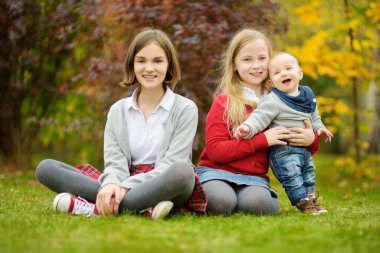 İki abla ve küçük erkek kardeşleri dışarıda eğleniyorlar. İki genç kız yaz günü erkek kardeşlerini kucağında tutuyorlar. Geniş yaş farkı olan çocuklar. Kardeşler arasında büyük yaş farkı var. Büyük aile..