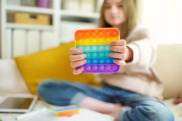 Teenage girl playing with rainbow pop-it fidget toy while studying at home. Teen kid with trendy stress and anxiety relief fidgeting game. Popping the dimples of sensory silicone toy.