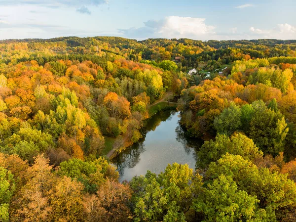 Birds eye view of autumn forest and a small lake. Aerial colorful forest scene in autumn with orange and yellow foliage. Fall scenery near Vilnius, Lithuania.