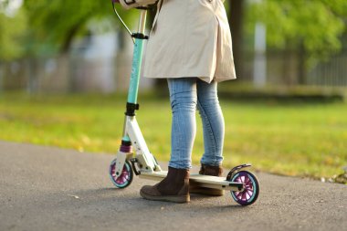 Güneşli bir sonbahar akşamında şehir parkında motosikletine binen genç bir kız. Çocuk tekerlekli sandalyeye biniyor. Çocuklar için aktif eğlence ve açık hava sporu.