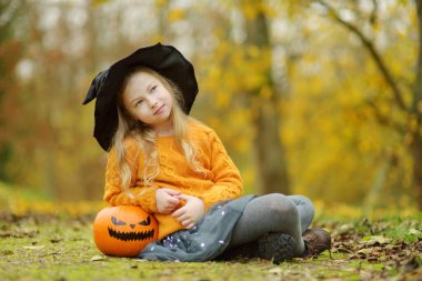 Siyah cadı şapkası takan sevimli genç bir kız elinde küçük bir balkabağı tutuyor. Cadılar Bayramı 'nda çocuk şakası mı şeker mi? Şükran Günü ve Cadılar Bayramı 'nda aile zamanı. Ekim 'de festival sezonu.