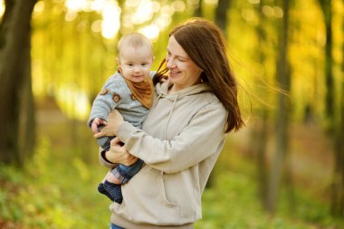 Annesinin kollarında tatlı bir erkek bebek. Anne ve oğlu güneşli bir sonbahar gününde şehir parkında eğleniyorlar. Sevimli oğlu annesi tarafından tutuluyor..