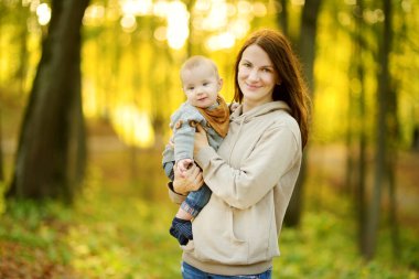 Annesinin kollarında tatlı bir erkek bebek. Anne ve oğlu güneşli bir sonbahar gününde şehir parkında eğleniyorlar. Sevimli oğlu annesi tarafından tutuluyor..