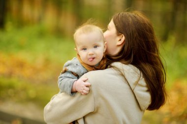Annesinin kollarında tatlı bir erkek bebek. Anne ve oğlu güneşli bir sonbahar gününde şehir parkında eğleniyorlar. Sevimli oğlu annesi tarafından tutuluyor..