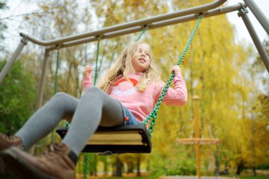 Güzel bir sonbahar parkında oyun parkında eğlenen güzel bir genç kız. Sonbaharın sonlarında dışarıda oynayan tatlı bir çocuk. Çocuklu aileler için açık hava aktiviteleri.