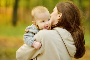 Annesinin kollarında tatlı bir erkek bebek. Anne ve oğlu güneşli bir sonbahar gününde şehir parkında eğleniyorlar. Sevimli oğlu annesi tarafından tutuluyor..