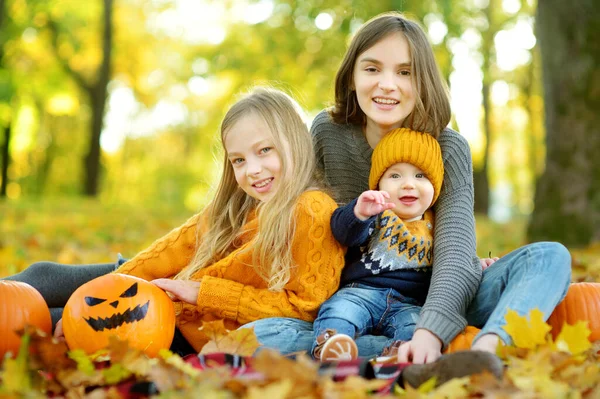 在阳光明媚的秋日 两个可爱的小女孩和她们的小弟弟抱着一个小南瓜 脸上涂满了恐怖的图画 孩子们在万圣节欺骗或治疗 万圣节的家庭时间 — 图库照片